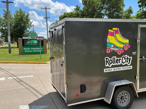 A mobile skating program trailer parked near the Osage Community School District sign on a sunny day.