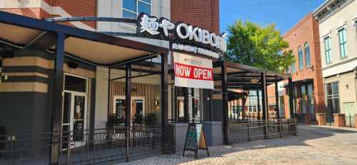 Exterior of Okibō Ramen restaurant with a "NOW OPEN" sign, featuring a modern design and outdoor seating area.
