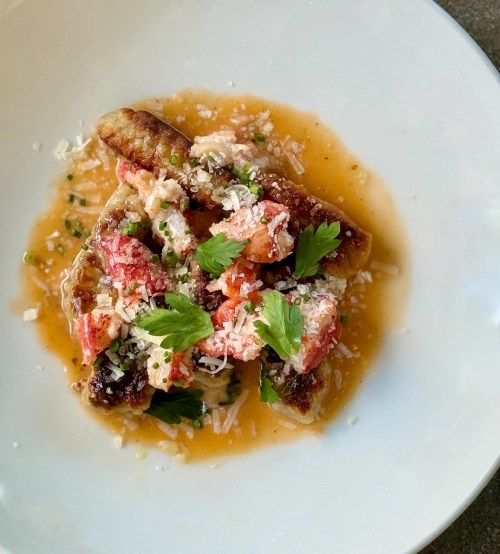 A plate of lobster with herbs and cheese, served on a bed of sauce, garnished with parsley.