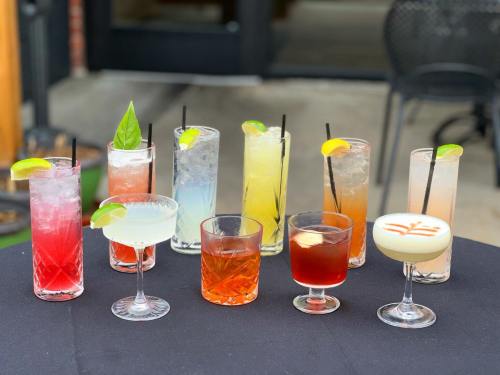 A variety of colorful cocktails arranged on a table, featuring garnishes like lime, lemon, and basil.