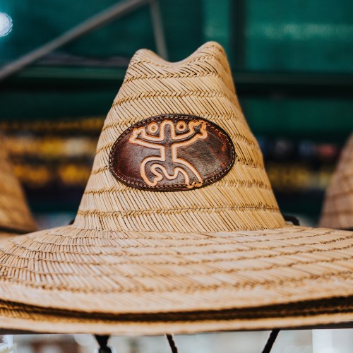 A close-up of a woven straw hat featuring a decorative emblem with a stylized figure.