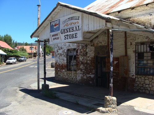 A weathered general store with a Pepsi sign, located on a quiet street in a small town.