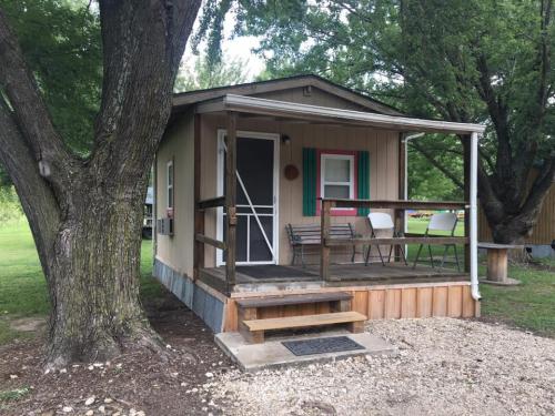 A small cabin with a porch, surrounded by trees and grass, featuring colorful shutters and outdoor seating.