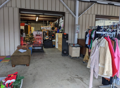 A cluttered garage space with clothing racks, a couch, and holiday decorations in the background.