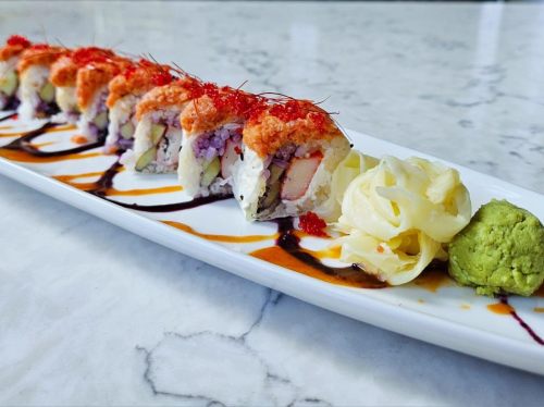 A plate of colorful sushi rolls topped with fish roe, accompanied by pickled ginger and wasabi on a marble surface.