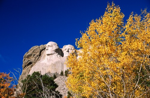 Mount Rushmore with autumn foliage in the foreground against a clear blue sky.