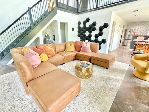 A modern living room featuring a large tan sectional sofa with colorful pillows, a geometric coffee table, and stylish decor.