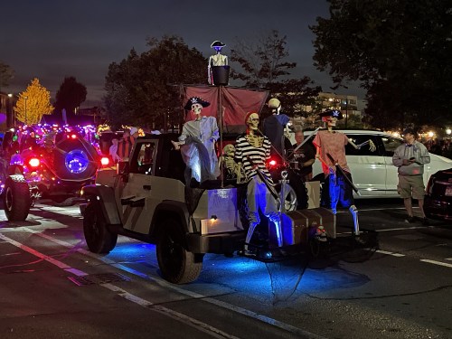 A decorated vehicle with skeletons dressed as pirates, illuminated by colorful lights, in a festive nighttime parade.