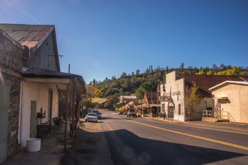 A quiet street in a small town, featuring rustic buildings and a clear blue sky.