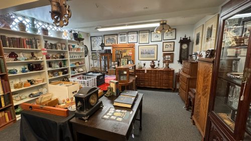 A cozy antique shop filled with vintage furniture, collectibles, and framed artwork on the walls.