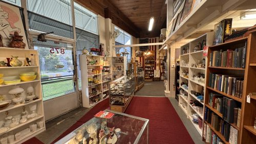A cozy antique shop aisle lined with shelves of collectibles, books, and decorative items, with a display case in the foreground.