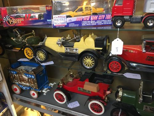 A display of vintage toy cars in various colors and styles, including a yellow car and a red fire truck.