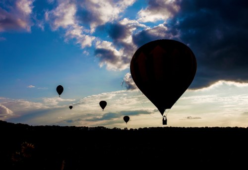 Silhouetted hot air balloons float against a colorful sunset sky with clouds.