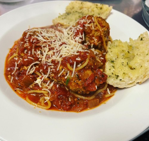 A plate of spaghetti and meatballs topped with marinara sauce and grated cheese, served with garlic bread.