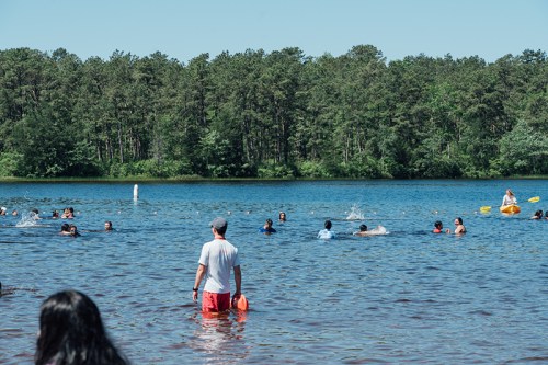 A sunny day at a lake with people swimming and kayaking, surrounded by trees and clear blue water.
