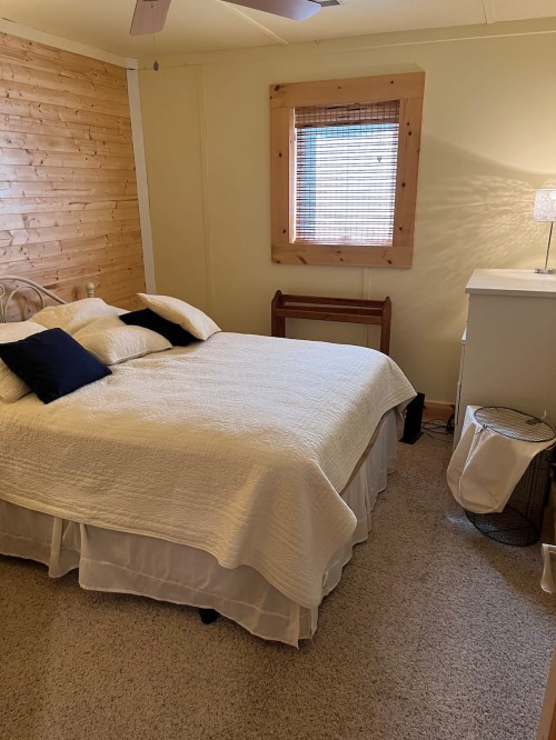Cozy bedroom with a bed, decorative pillows, wooden accents, and a window with natural light.