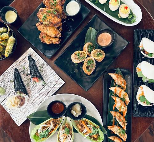 A variety of colorful dishes including wings, dumplings, sushi rolls, and appetizers arranged on elegant plates.