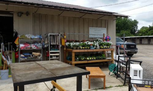 A garden shop exterior with potted flowers, a wooden display, and various items for sale outside a building.