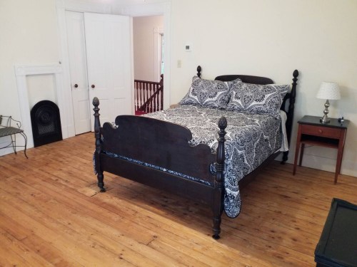 A cozy bedroom featuring a dark wooden bed with a patterned blanket, a nightstand, and wooden flooring.