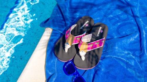 A pair of colorful flip-flops on a blue towel by a pool, with sunglasses nearby.