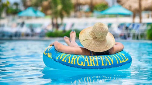 A person relaxes on a blue inflatable tube in a pool, wearing a large straw hat.