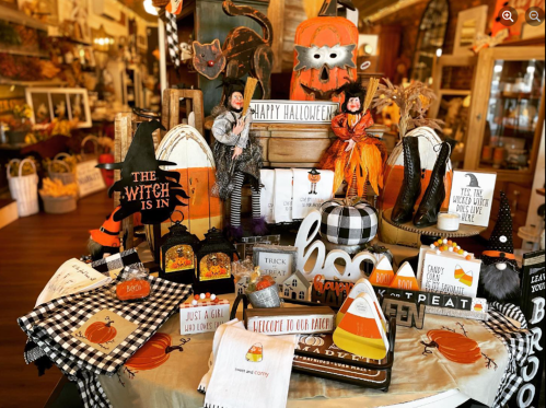 A festive display of Halloween decorations, including pumpkins, witches, and themed signs, in a cozy shop setting.