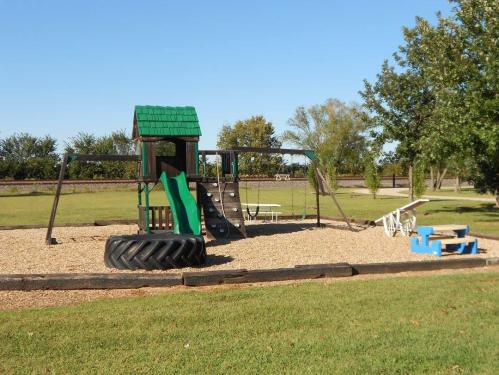 A playground with a green-roofed play structure, slide, swings, and a tire, set in a grassy area.