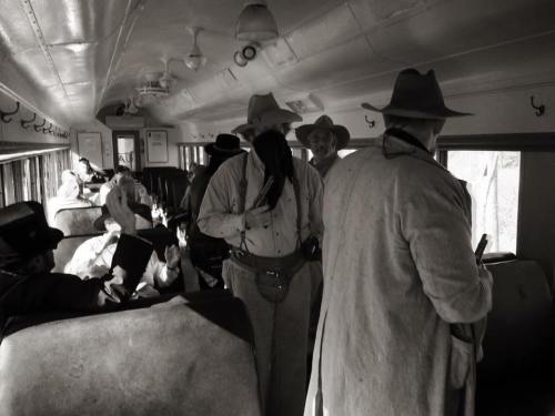 A group of people in vintage clothing and hats inside an old bus, some seated and others standing.