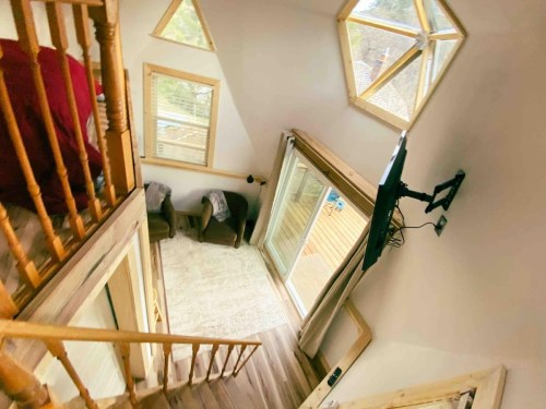A cozy interior view from above, featuring a staircase, large windows, and a living area with two chairs and a TV.