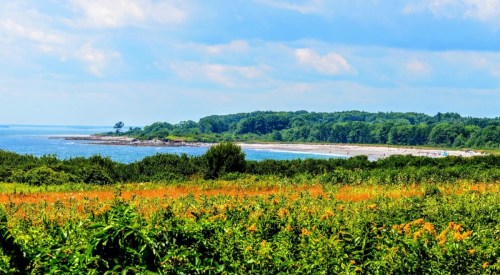 A scenic view of a beach surrounded by lush greenery and blue waters under a partly cloudy sky.