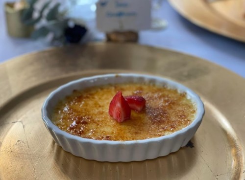 A creamy crème brûlée topped with fresh strawberries, served in a white dish on a gold plate.