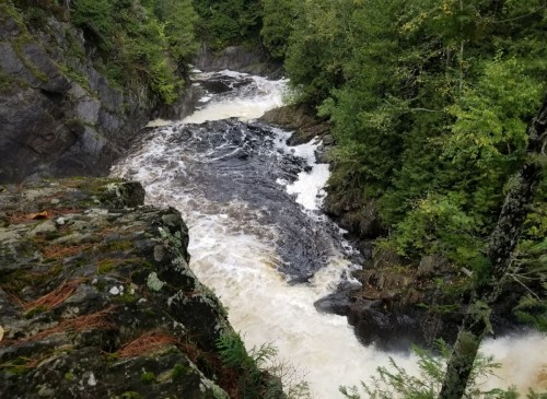 A rushing river flows through rocky terrain, surrounded by lush green trees and steep cliffs.