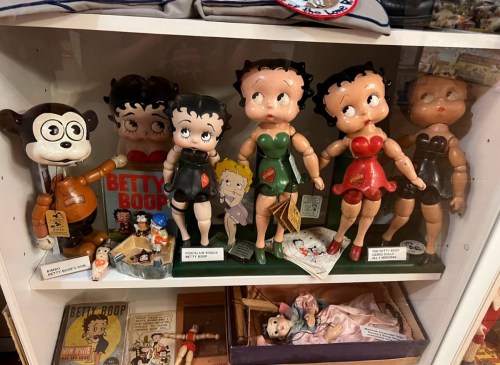 A display of vintage Betty Boop dolls and memorabilia, featuring various dolls in different outfits and a cartoon dog.