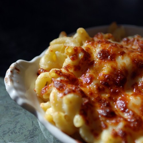 A close-up of baked macaroni and cheese in a white dish, with a golden, crispy cheese topping.