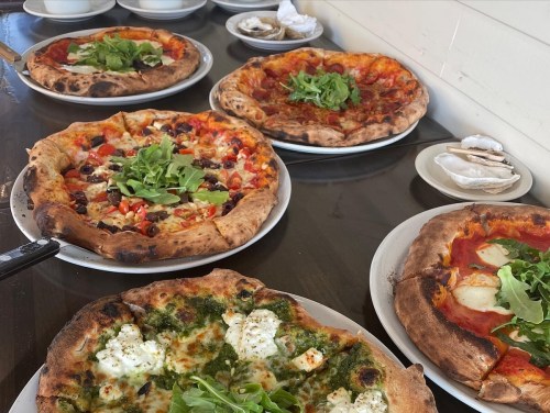 A table with five pizzas, each topped with various ingredients like arugula, cheese, and vegetables.