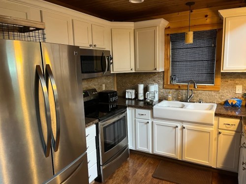 A modern kitchen featuring stainless steel appliances, white cabinets, and a farmhouse sink with wooden accents.