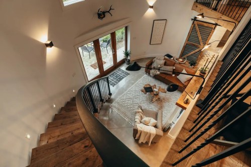 A modern, open staircase leads to a cozy living area with a sofa, plants, and large windows overlooking a patio.