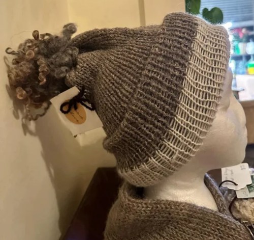 A knitted hat with a curly pom-pom on top, displayed on a mannequin head.