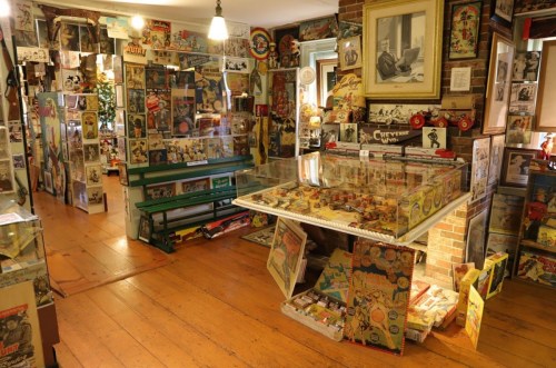 A vintage-themed room filled with memorabilia, posters, and collectibles, featuring a display table and wooden flooring.