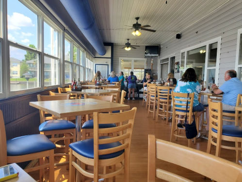 A bright, casual dining area with wooden tables and chairs, featuring patrons enjoying their meals by large windows.