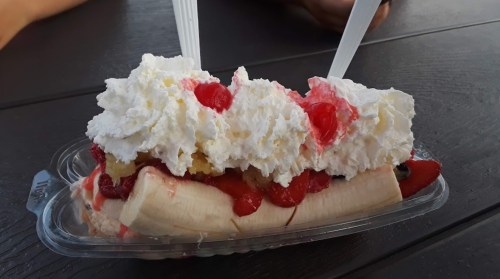 A banana split topped with whipped cream, cherries, and various fruit toppings in a clear container.