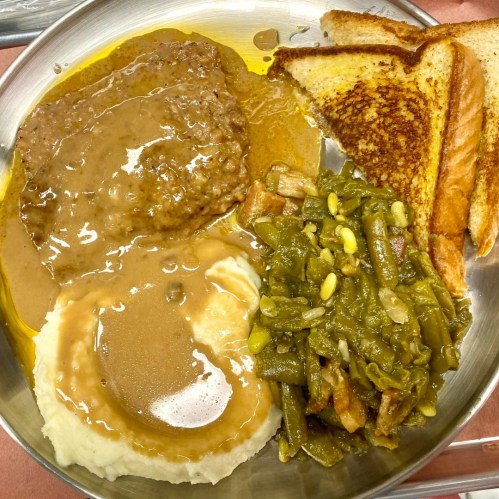 A metal plate with meatloaf and gravy, mashed potatoes, green beans, and toasted bread.