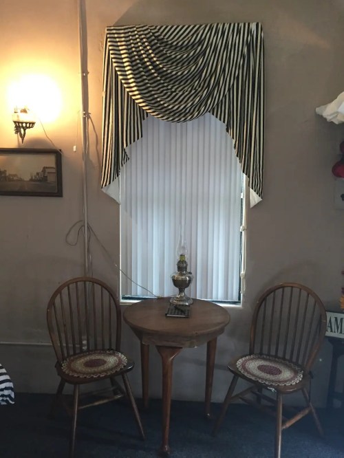 A cozy corner with a striped curtain, a small round table, and two wooden chairs, illuminated by soft light.