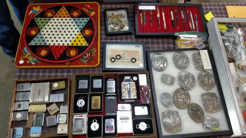 A display of vintage items including a game board, pens, lighters, and silver accessories on a table.