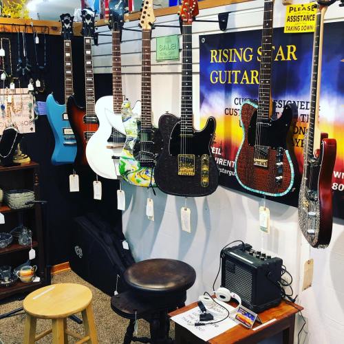 A display of various guitars hanging on a wall, with a stool and amplifier in front, at a music shop.