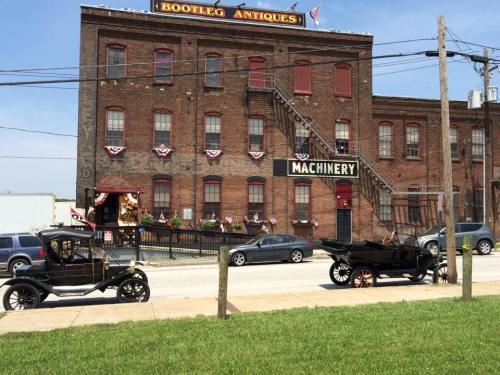Historic brick building with "Bootleg Antiques" sign, vintage cars parked in front, and decorative bunting.