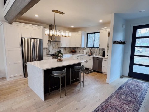 Modern kitchen with white cabinets, a large island, stainless steel appliances, and a stylish light fixture.