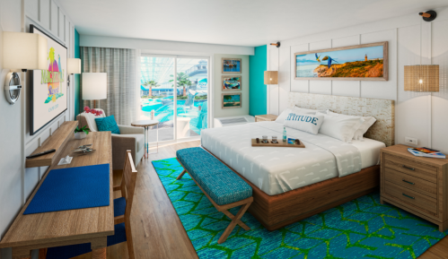 Brightly decorated hotel room with a king bed, desk, and large window overlooking a pool area. Colorful accents throughout.