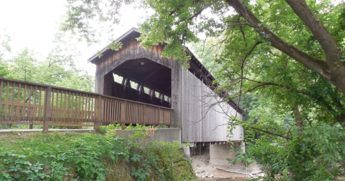 A wooden covered bridge is surrounded by green trees and shrubbery in Michigan.