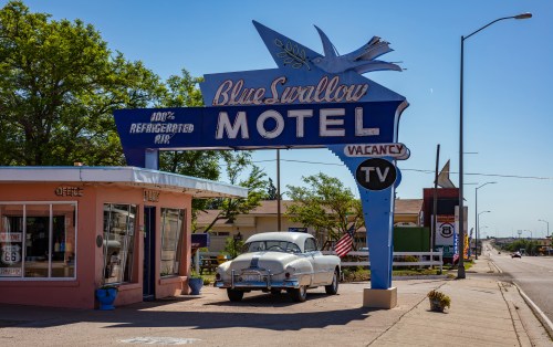 otel Blue Swallow next to mother road, route 66, a sunny day. An antique car is parked at the entrance.